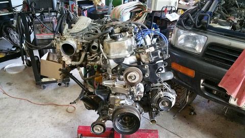 Toyota V6 engine dressed and ready on an engine stand next to the truck it came from, in Rob's shop