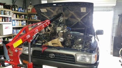 Toyota 4Runner in the shop with the hood up and a red engine hoist lifting the engine out